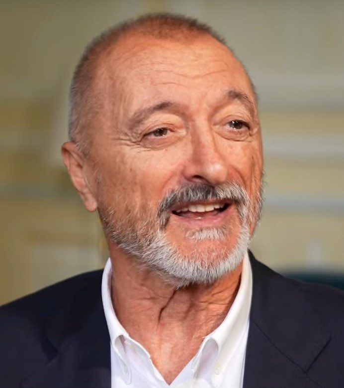 Author portrait — Arturo Pérez-Reverte, seated, in low warm light